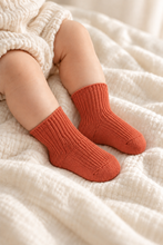 Load image into Gallery viewer, Baby wearing terracotta ribbed organic baby socks on a soft cream blanket